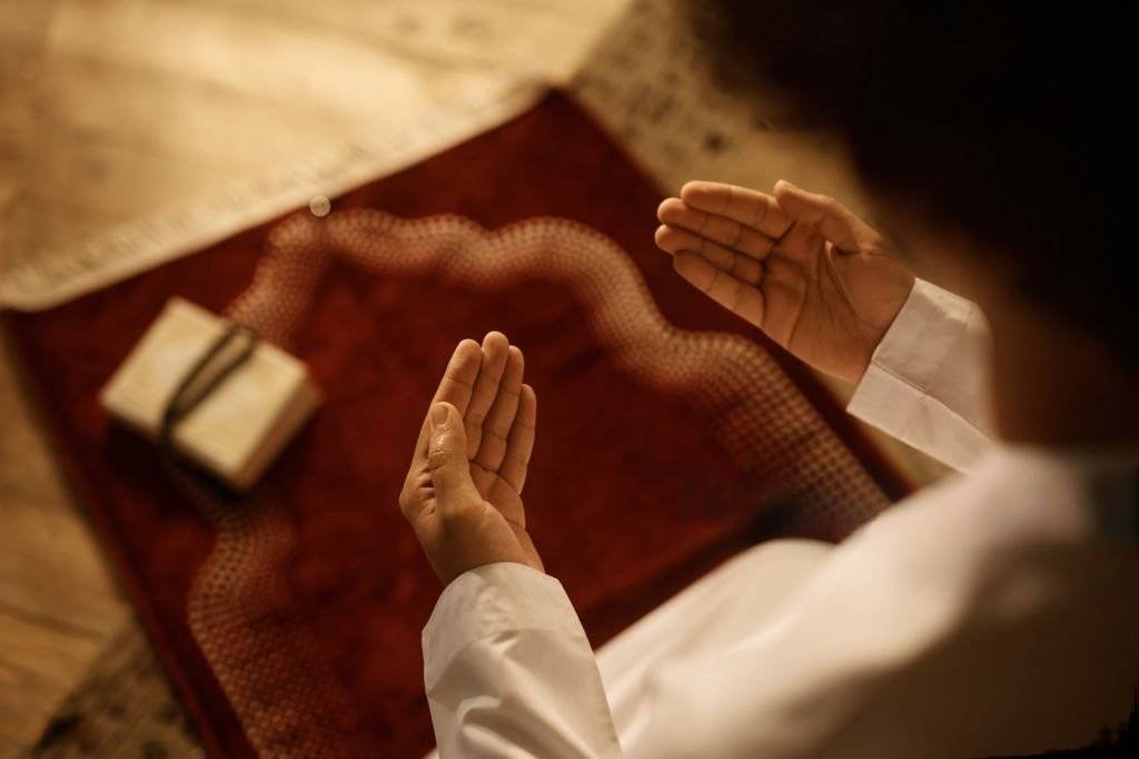 A man sits on a prayer mat and asks God for help to control his self.