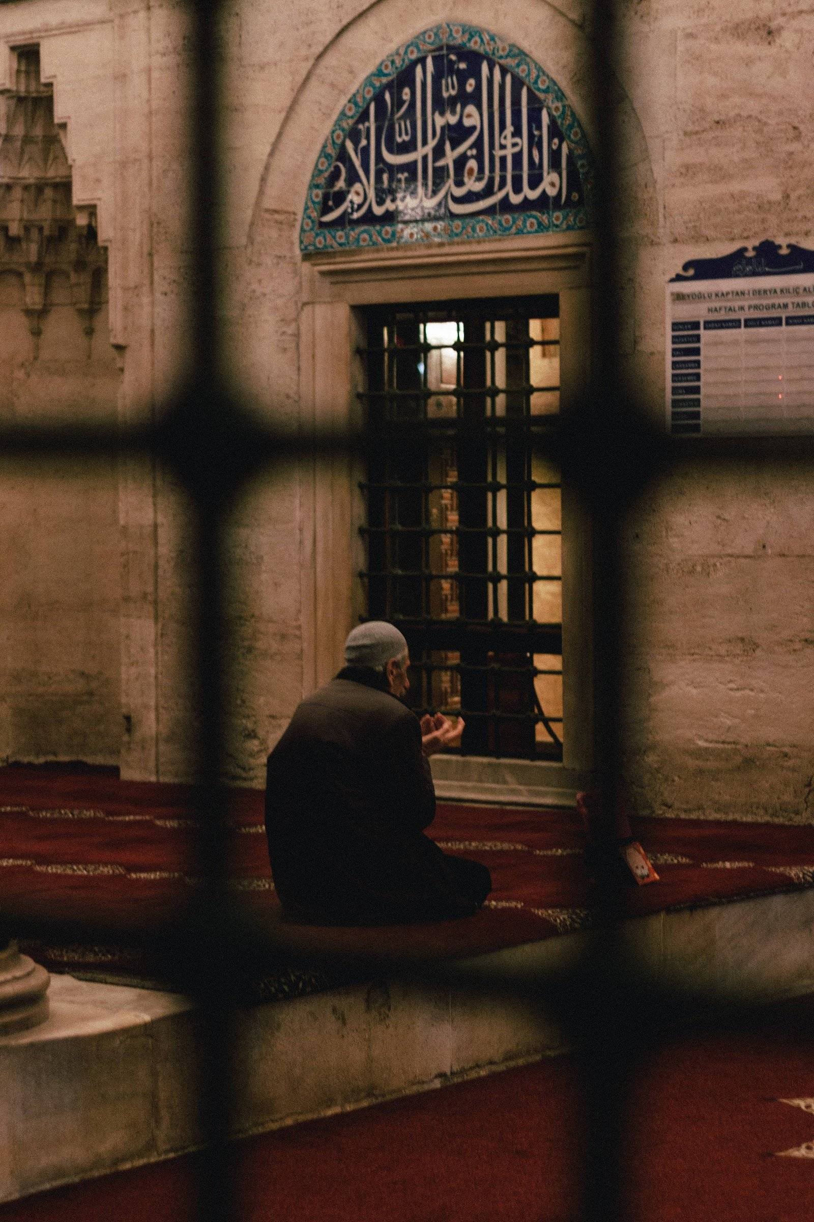 A man is sitting on the ground in a mosque praying for forgiveness.