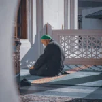 An elderly Muslim man in a green prayer cap, sitting in a mosque while seeking Laylat-ul-Qadr in the Last Ten Nights of Ramadan