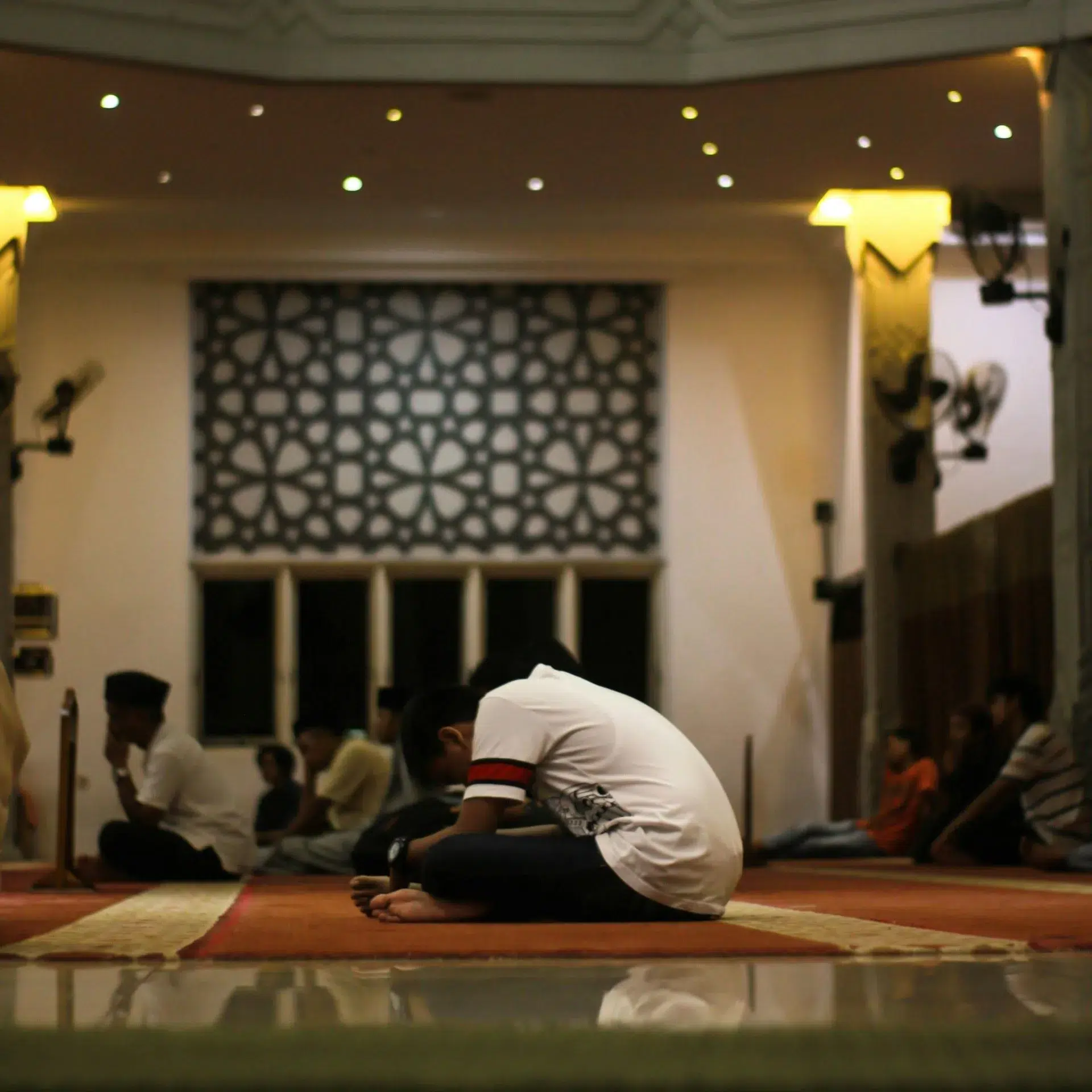 A person is sitting in contemplation and prayer in a mosque, embodying the reflective and devotional spirit of the Three Ashras of Ramadan.