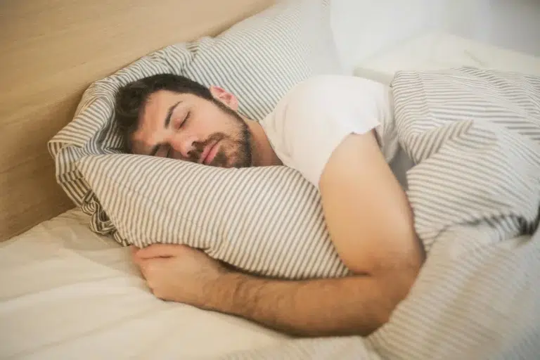 A man peacefully sleeping on a bed, resting his head on a striped pillow, with a calm and relaxed expression.