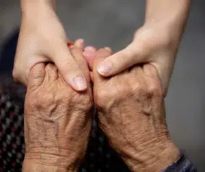 A younger person gently holding the hands of an elderly individual, symbolizing care, compassion, and support.