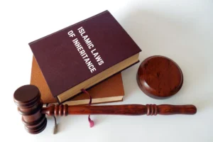 A book titled 'Islamic Laws of Inheritance' placed on top of another book with a wooden gavel and sound block beside them. The image represents the concept of Islamic inheritance laws and legal proceedings.