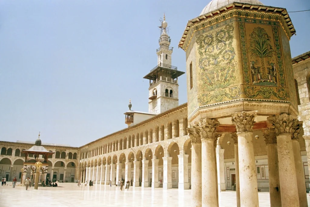 Courtyard view of the Great Mosque of Damascus, showcasing the intricate mosaic artwork, arched colonnades, and a towering minaret, exemplifying the architectural brilliance of early Islamic Umayyad architecture.