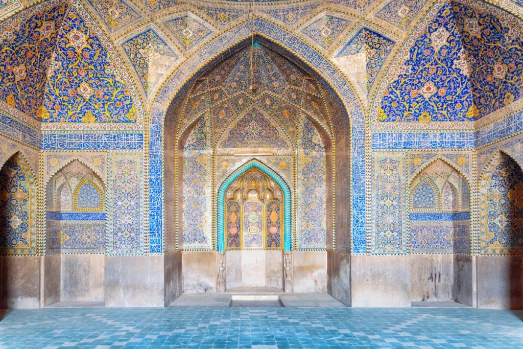 Intricate tile work and arched mihrab in the Isfahan Mosque, Iran, showcasing vibrant blue, gold, and turquoise geometric patterns and Arabic calligraphy, reflecting the stunning beauty of Persian Islamic architecture.