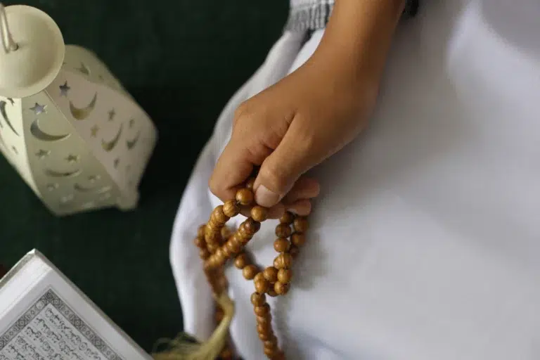 Person holding prayer beads while reading Quran as part of Ruqyah in Islam, a spiritual practice for healing and protection through reciting Quranic verses and making supplication.