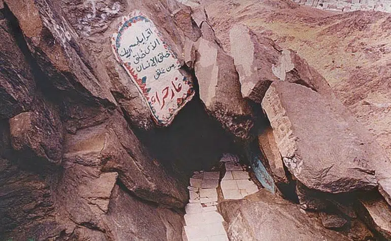 Entrance to the Cave of Hira on Jabal al-Nour, marked by a painted plaque with Arabic inscriptions, showing the rocky exterior and the small passage leading into the cave.