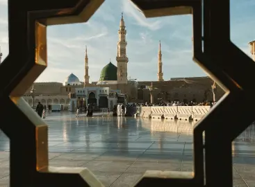 View of Masjid al-Nabawi in Madinah through an intricate geometric frame, featuring the iconic green dome and towering minarets under a clear blue sky.