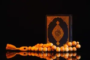 Elegant display of a Quran with intricate golden details, accompanied by wooden Muslim prayer beads (Tasbih) on a reflective surface, symbolizing spirituality and devotion.