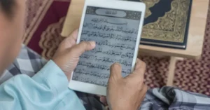 A Muslim man studying the Quran on a tablet at home, symbolizing flexible learning through the Best Online Quran Academies in the UK.